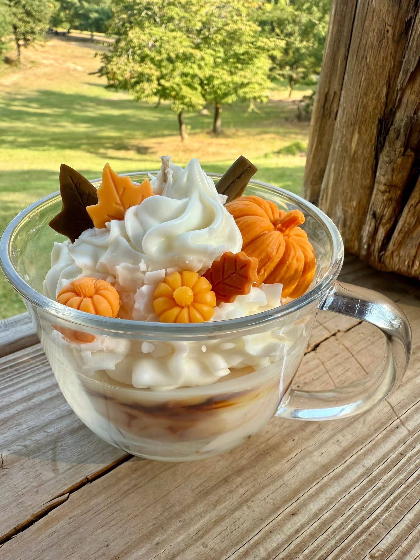 Whipped candle in a glass mug topped with wax pumpkins and fall leaves.